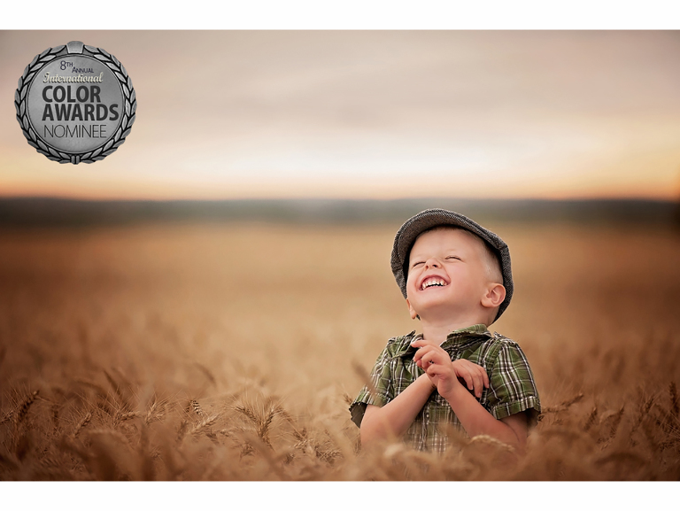 Young boy in a newsboy hat standing in a wheat field laughing with his head back.