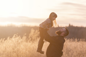A dad holds his little girl up in the air while he looks at her with outstretched arms