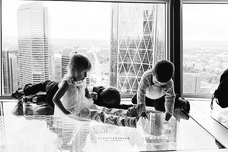 Three kids sit on the glass floor of the Calgary Tower looking 191 meters down.
