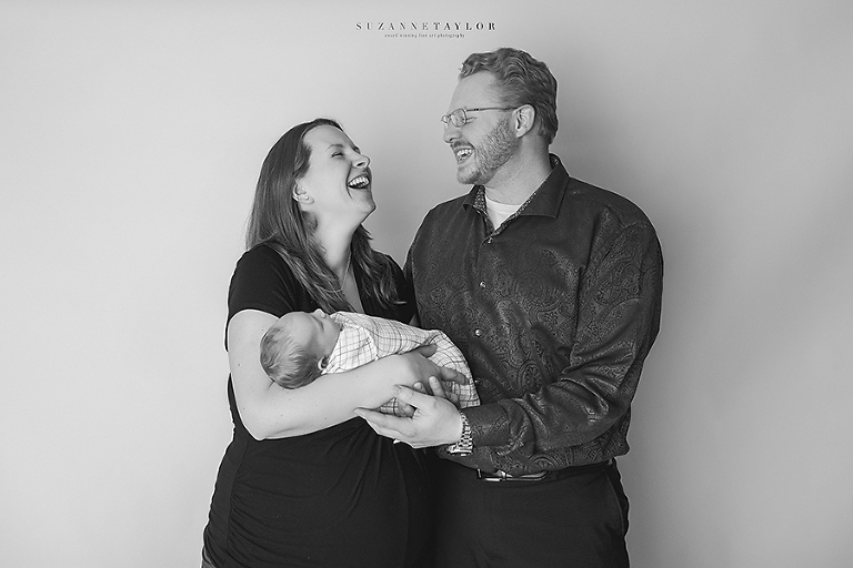 A mom and dad laugh together while holding their newborn baby son.