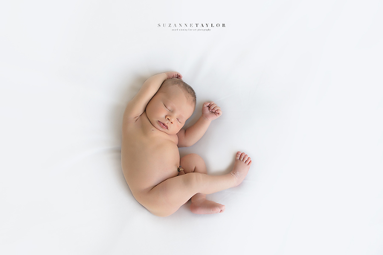 Baby boy laying on a white background rests while curled up for the Rock Your Bump show this October 15 in Red Deer, Alberta.