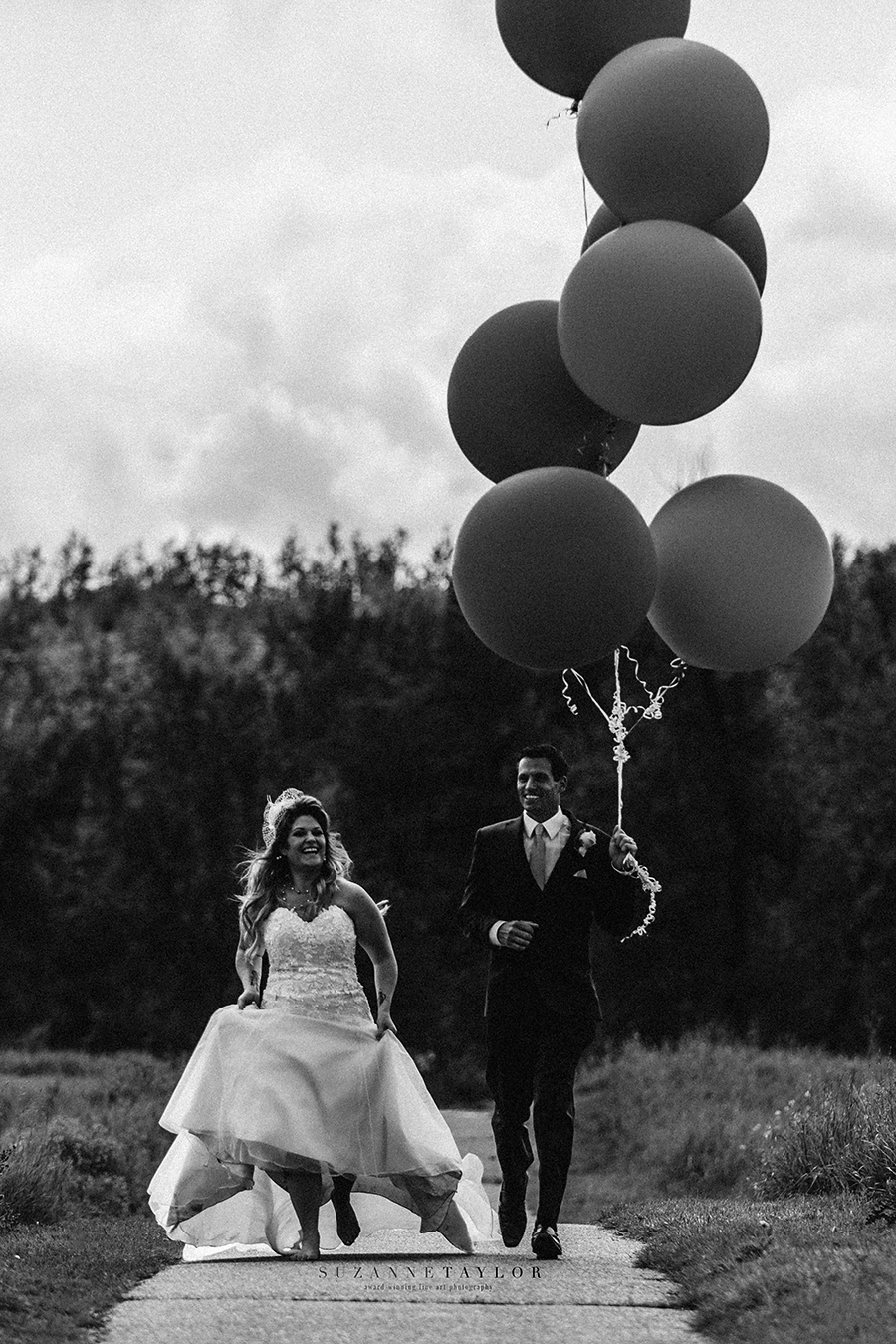 A newly married couple runs down a path with huge balloons trailing behind them during their Calgary Wedding.