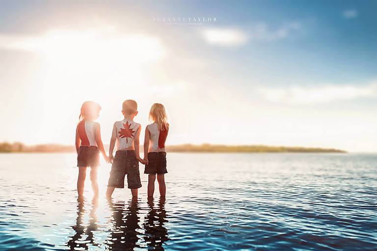 Triplets stand in Gull Lake, Alberta with the Canada Day Flag painted on their backs at sunset